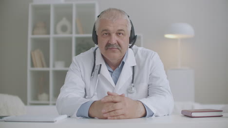 doctor-is-nodding-and-looking-at-camera-of-notebook-during-online-consultation-using-headphones-for-listening-patient-telemedicine-service
